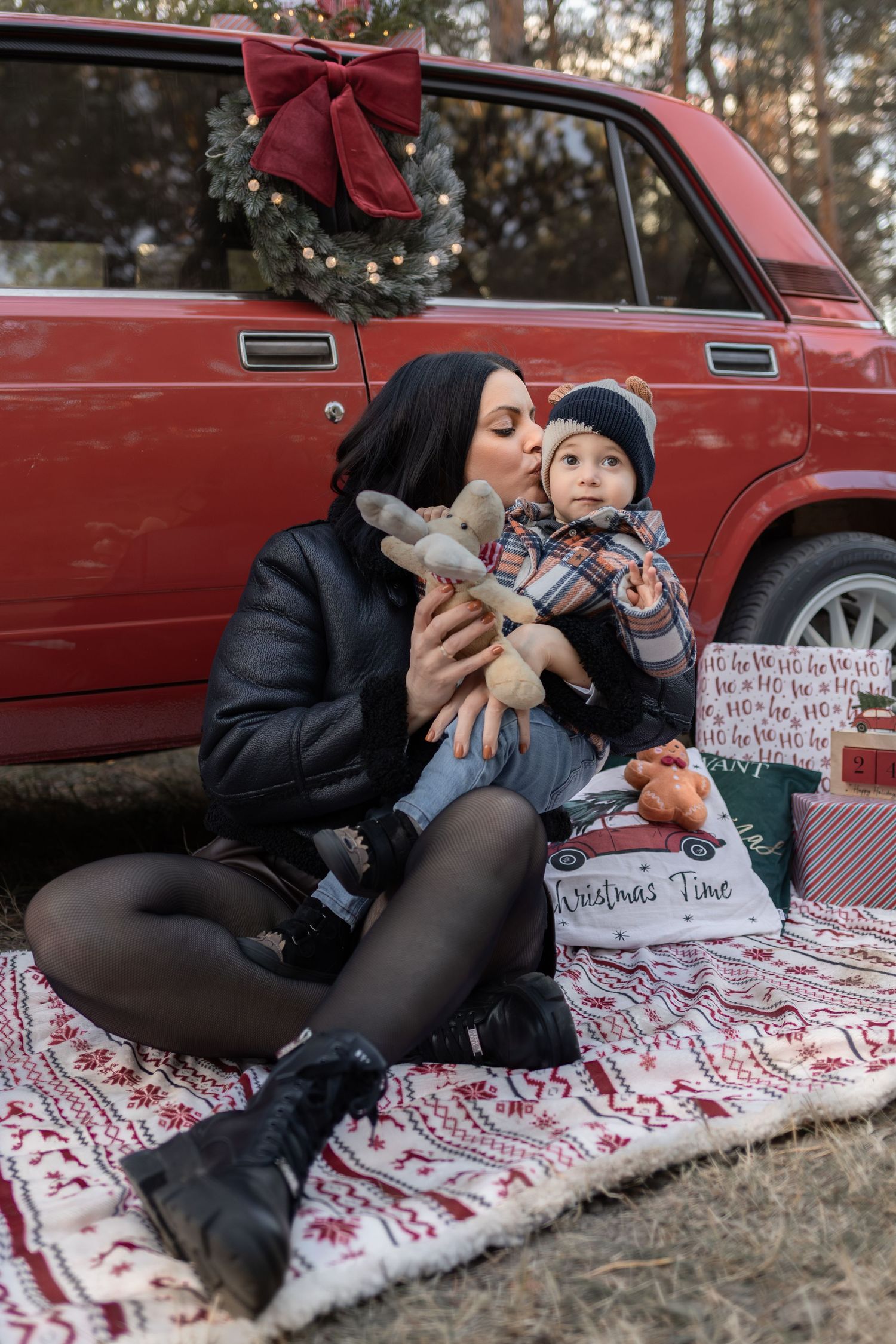 Anya és kisgyermeke szabadtéri karácsonyi fotózáson ölelkeznek a fenyőfák között Komarnoban.