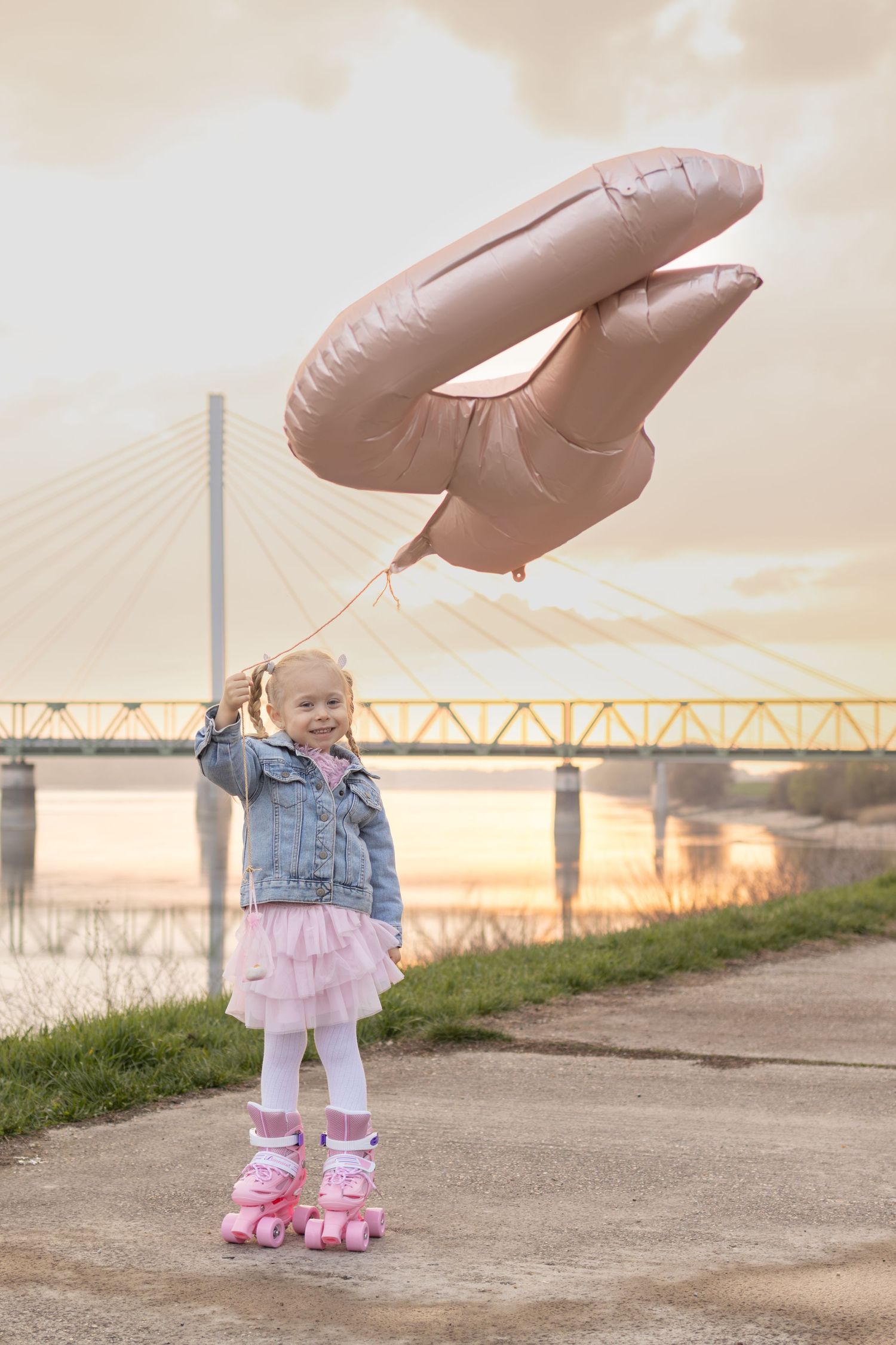 Toddler in denim and pink outfit near bridge during sunset.