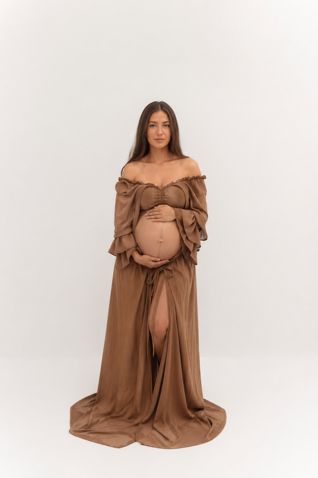 Pregnant woman in elegant brown off-shoulder maternity gown cradling baby bump, studio portrait on white background.