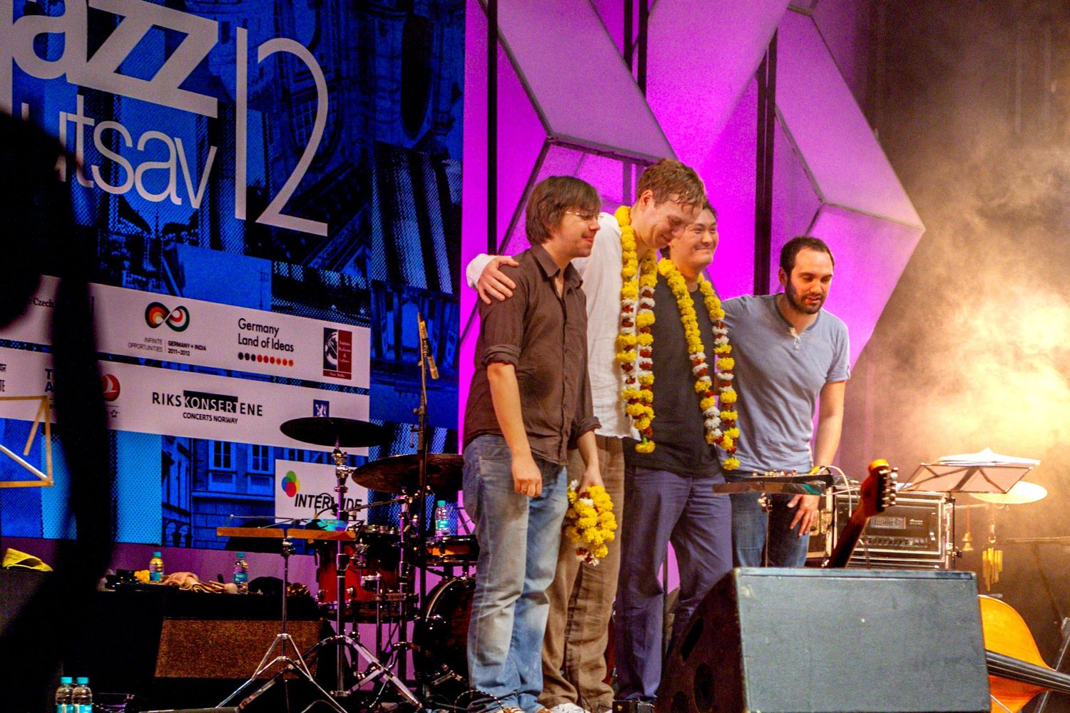 Musicians take a bow on stage at a jazz festival with purple lighting and performance equipment visible.