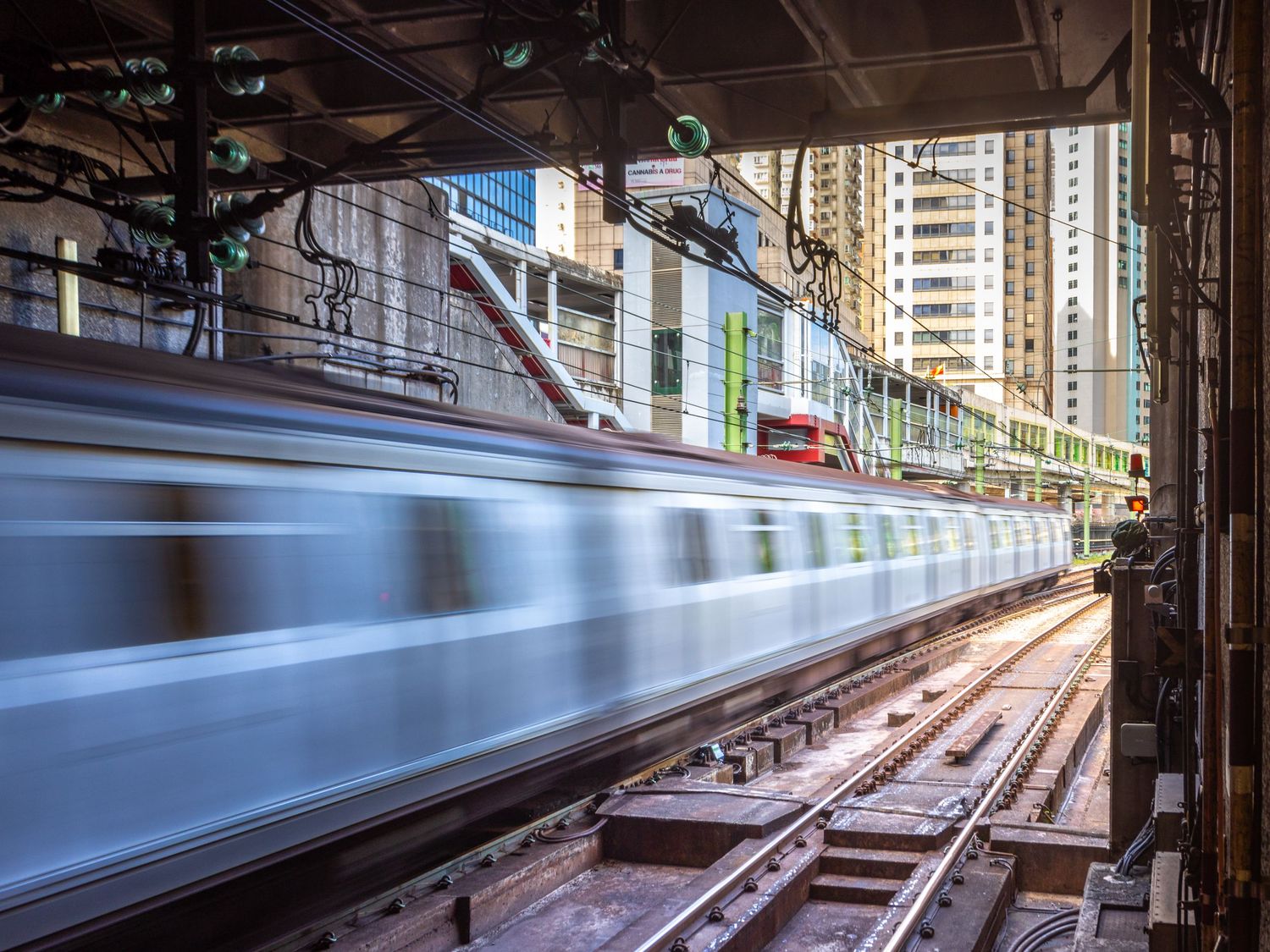 Motion-blurred subway train speeding through an urban station with buildings visible in background.