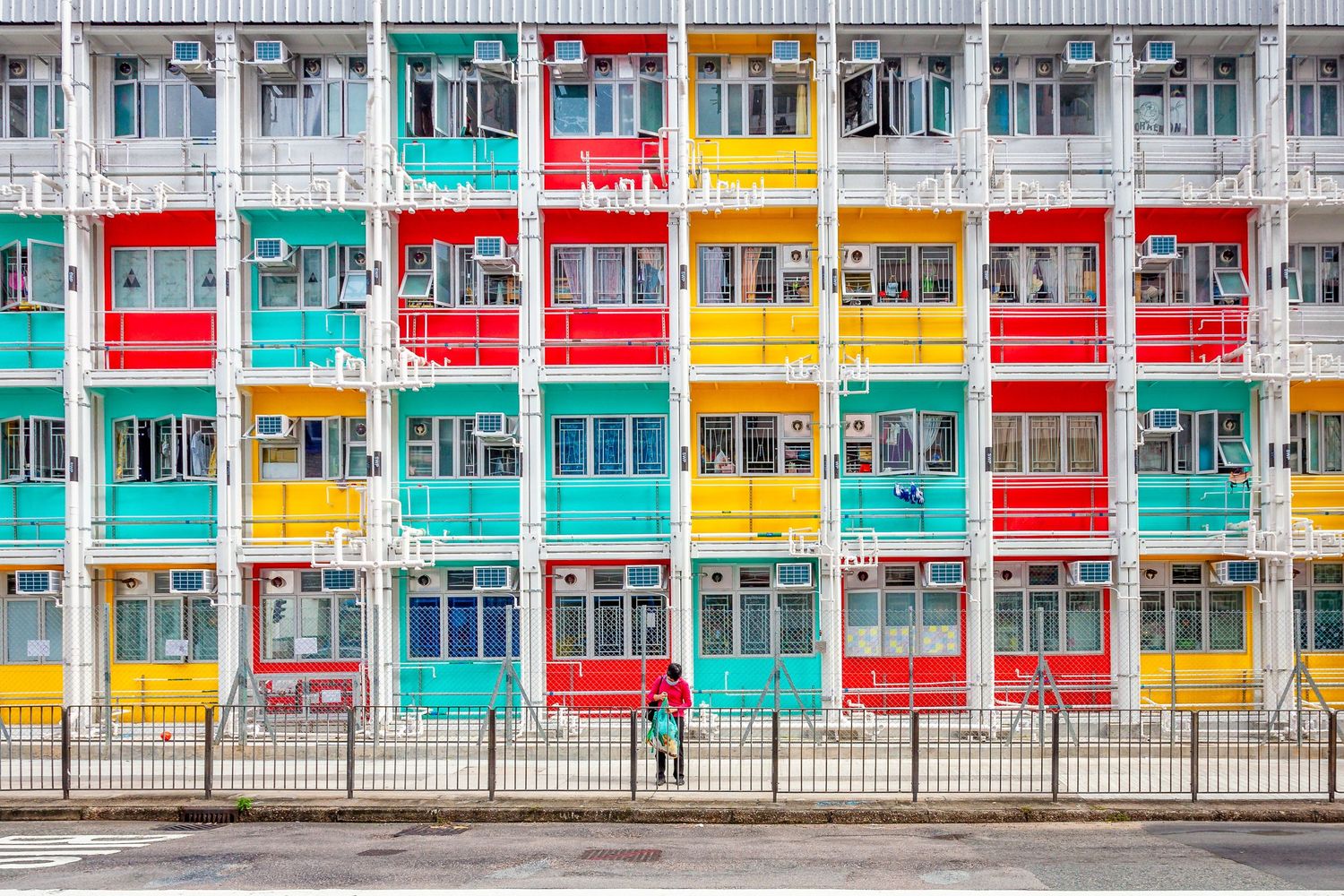 Colorful apartment building facade with turquoise, red, and yellow windows arranged in a geometric pattern.