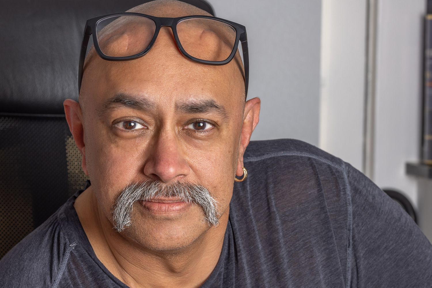 Middle-aged man with mustache and black glasses on head wearing gray t-shirt, close-up portrait photo.