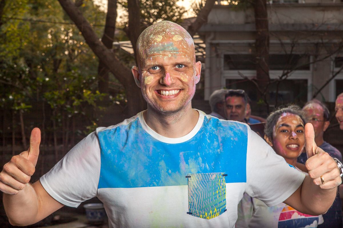 Festival participant covered in blue powder giving thumbs up during Holi celebration.