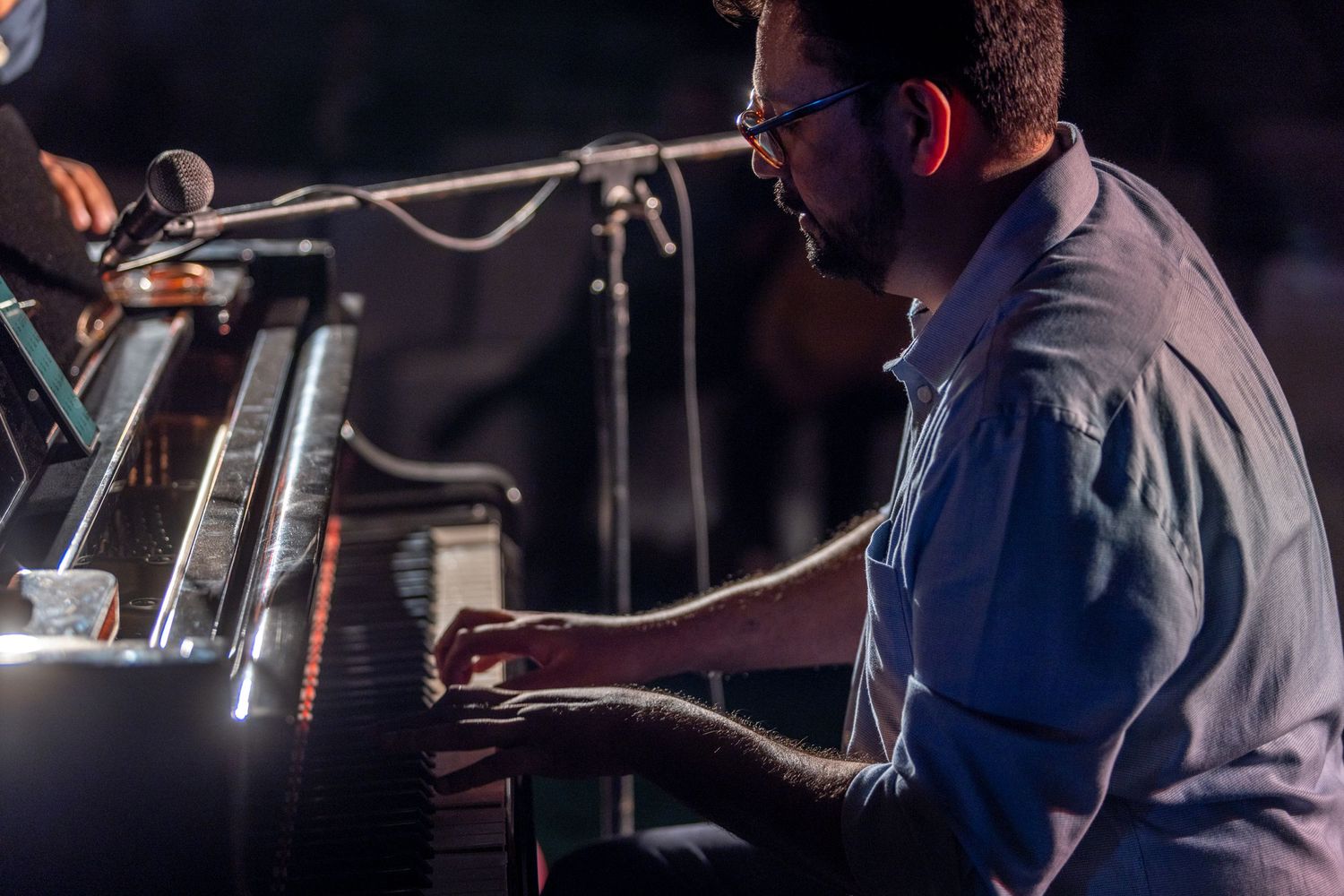 Pianist performing at grand piano during live concert with professional lighting setup.
