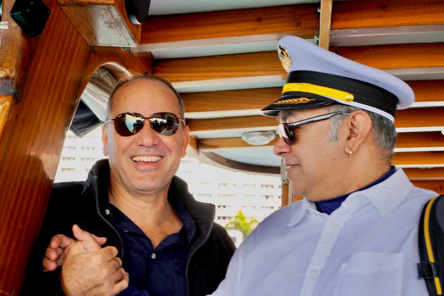 Two people sharing a laugh on a boat deck under wooden beams.