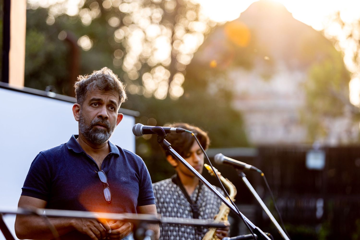 Musician performs at an outdoor venue during golden hour with microphone and equipment setup.