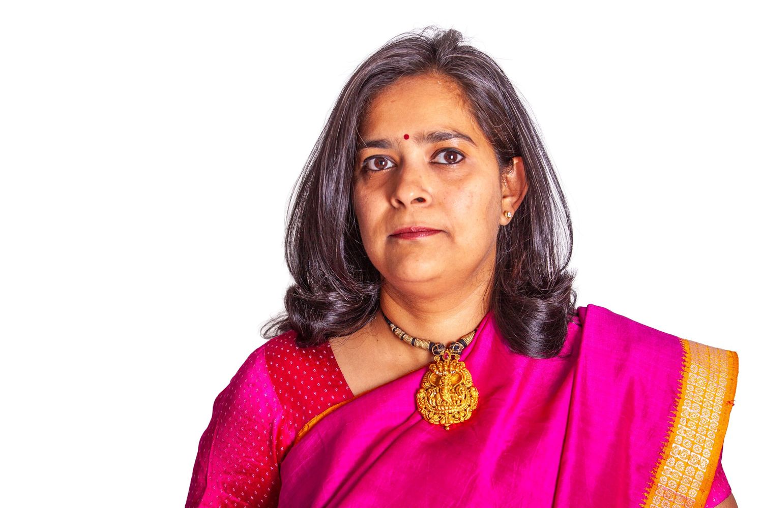 Woman in vibrant pink traditional Indian attire with gold jewelry and dark hair poses against white background.