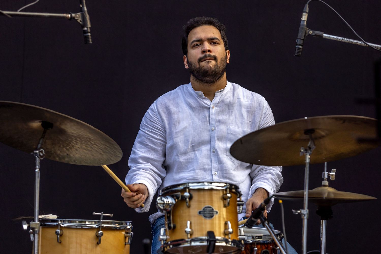 Drummer performs with concentration on a drum kit against a dark background.