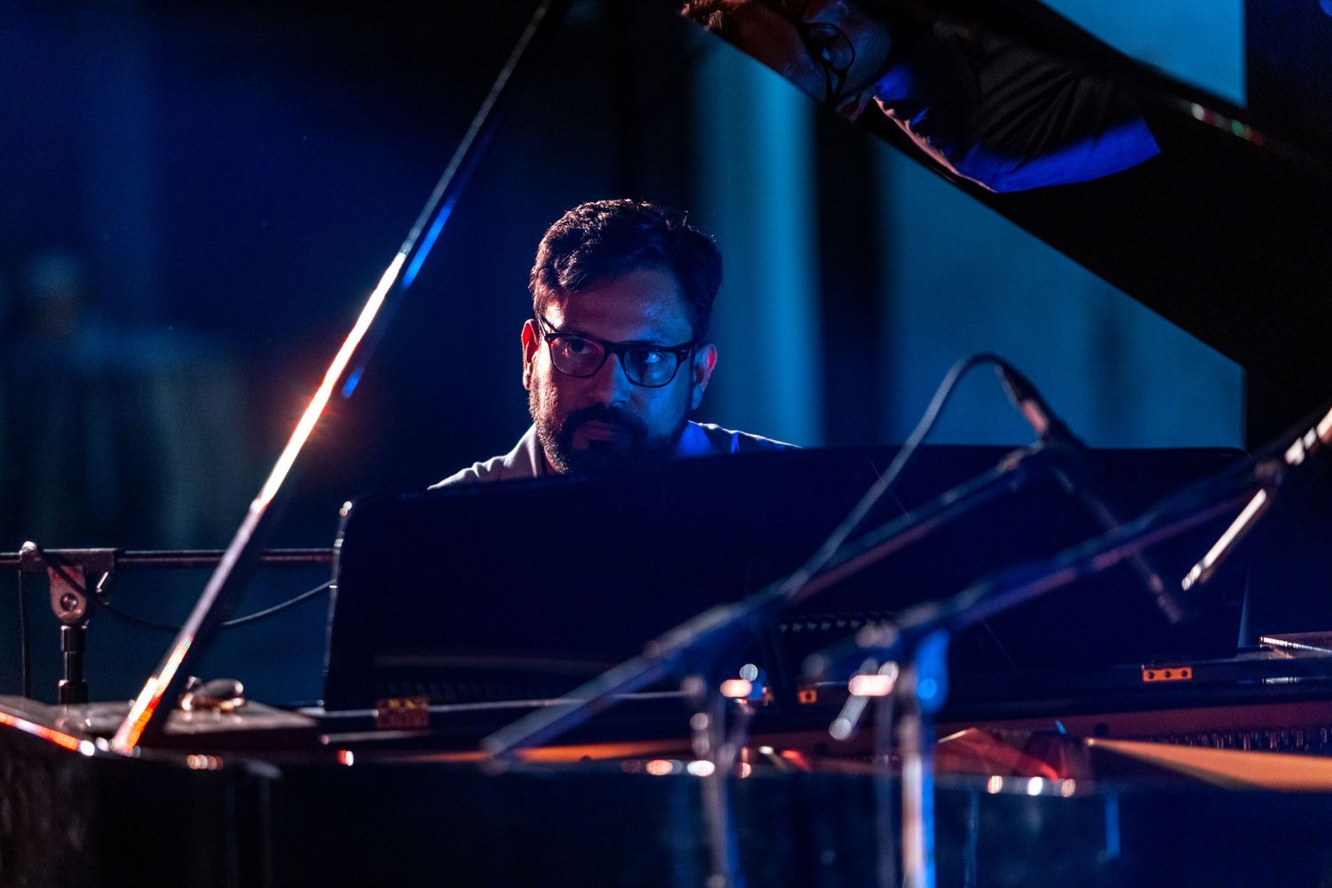 Pianist performs at a grand piano in moody blue lighting during a concert.
