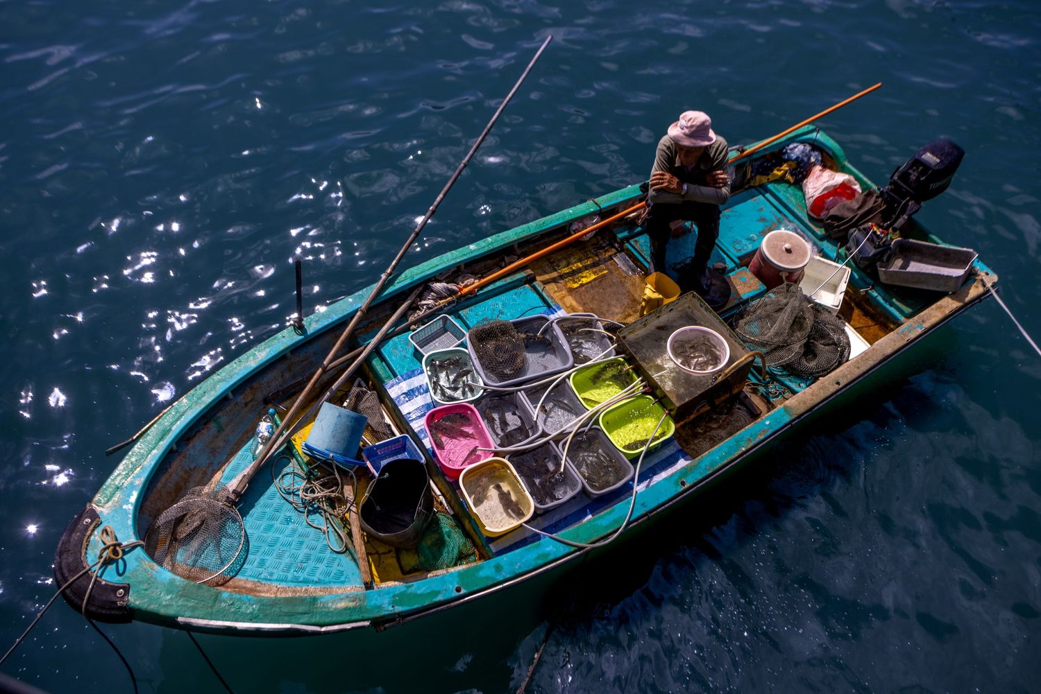 Aerial view of a small fishing boat filled with colorful containers on deep blue waters.