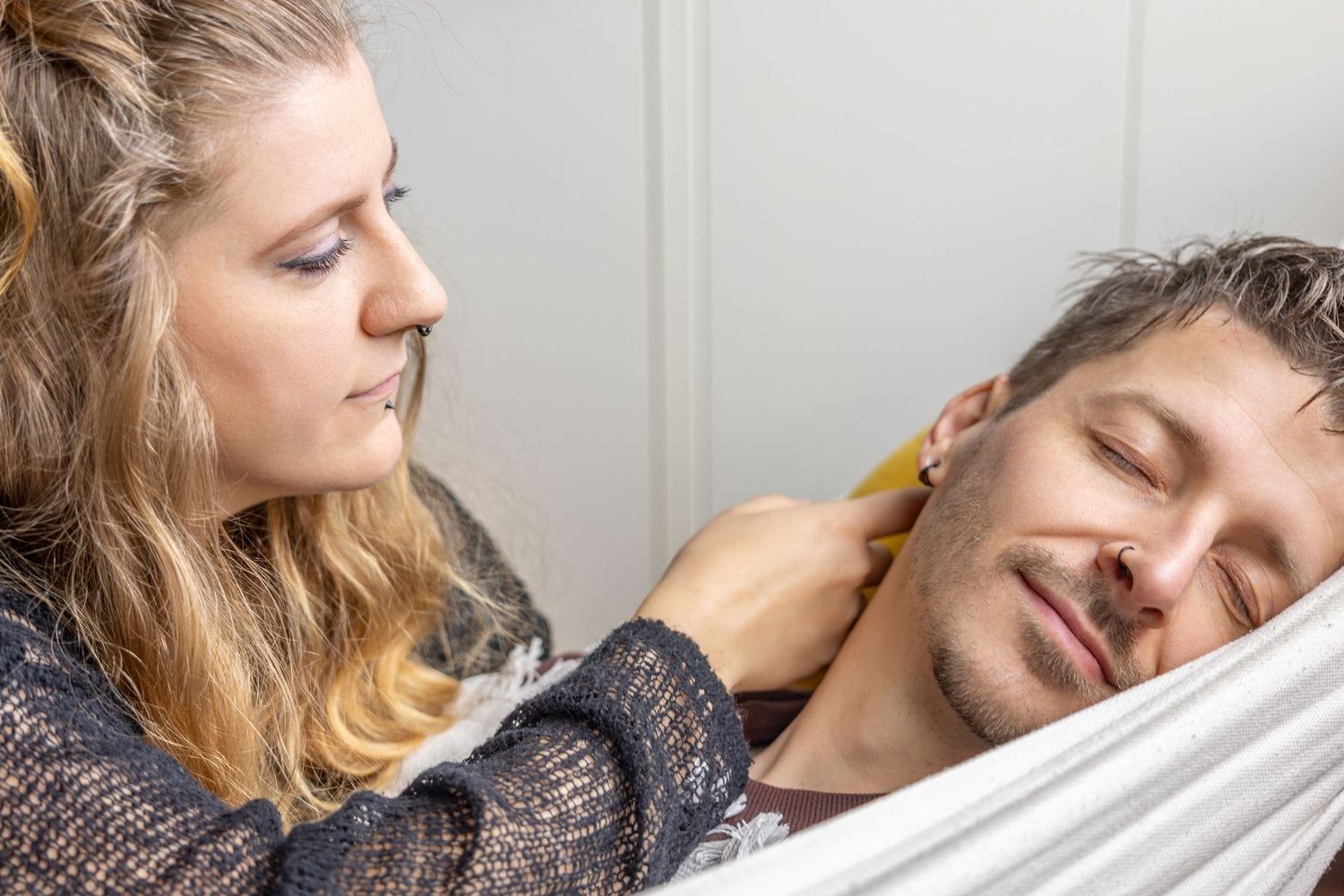 Woman gently touching sleeping man's face while he rests in a hammock indoors.