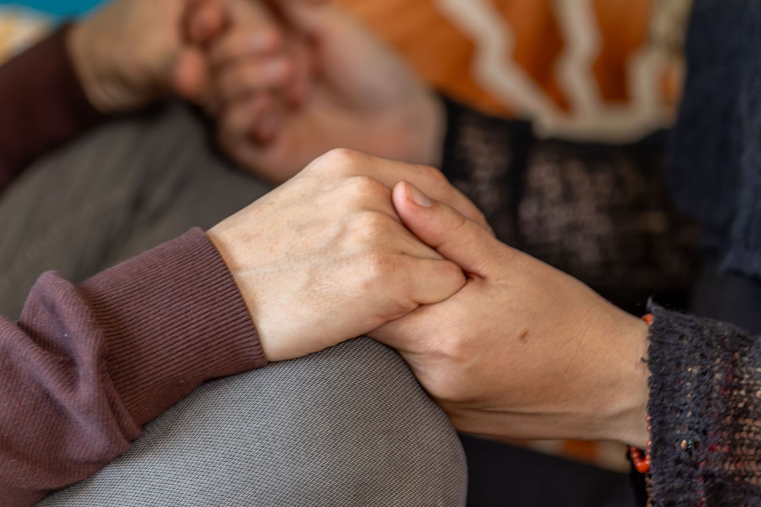 Two people holding hands in a comforting gesture, showing empathy and emotional support between generations.