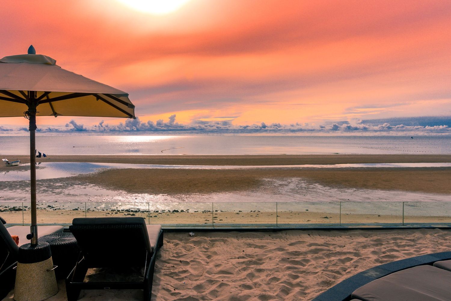 Beach chairs and umbrella silhouetted against a dramatic orange sunset over the ocean.