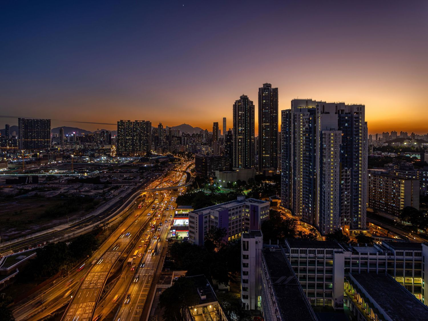 Dramatic sunset cityscape with illuminated skyscrapers and highway in warm golden light.