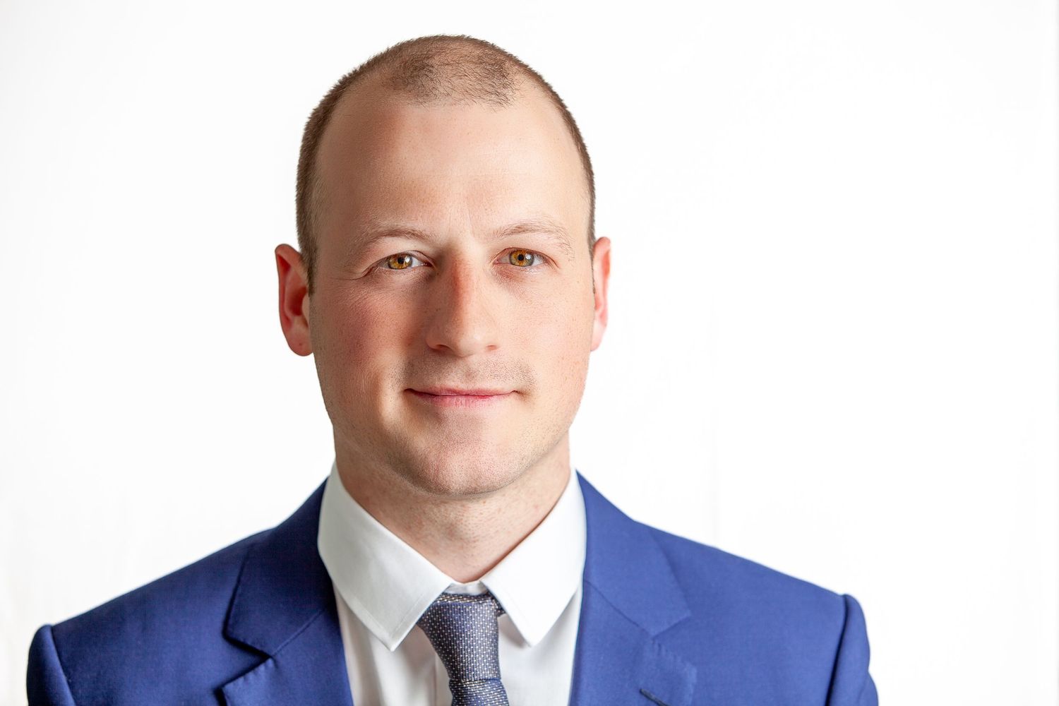 Professional headshot of person in blue suit and tie against white background.
