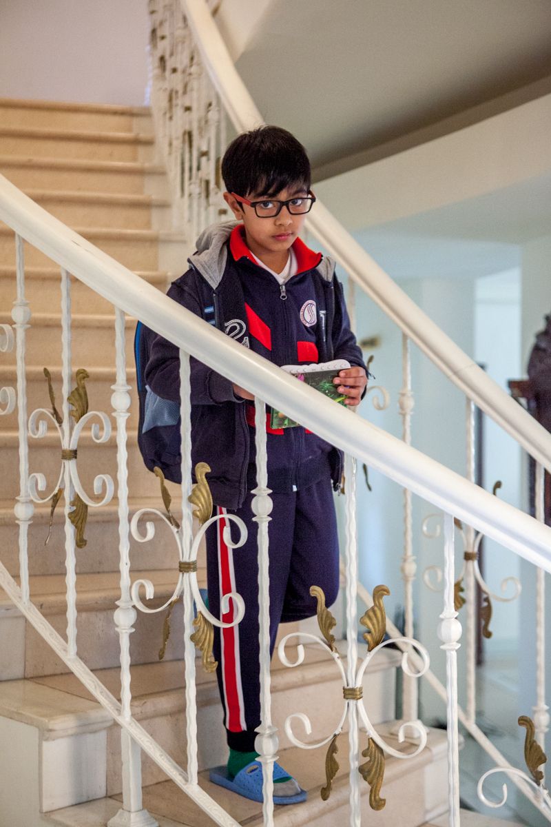 Student in school uniform standing on ornate white staircase while looking at mobile device.