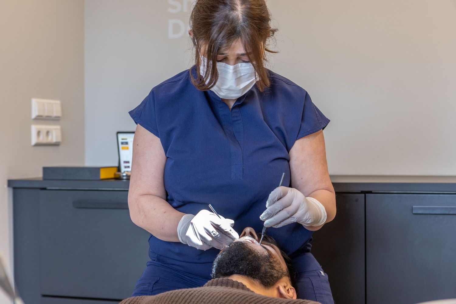 Dental professional in blue scrubs and protective gear working on patient.
