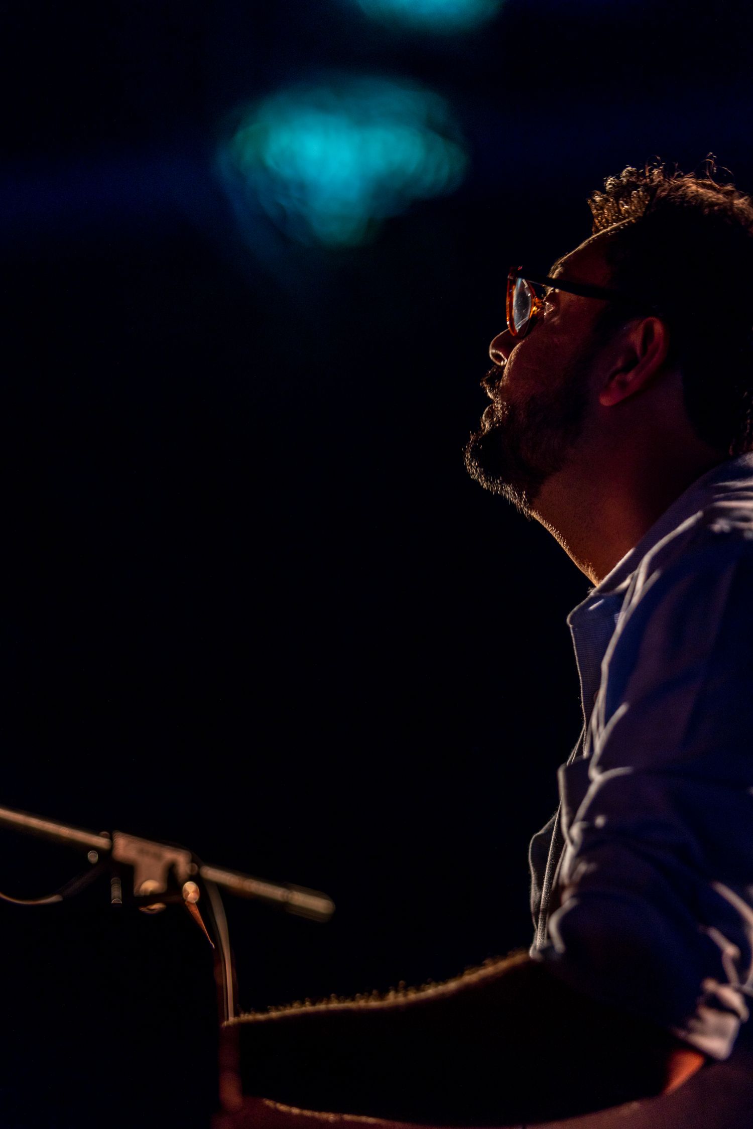 Side profile of musician at piano with ethereal blue lighting in background.