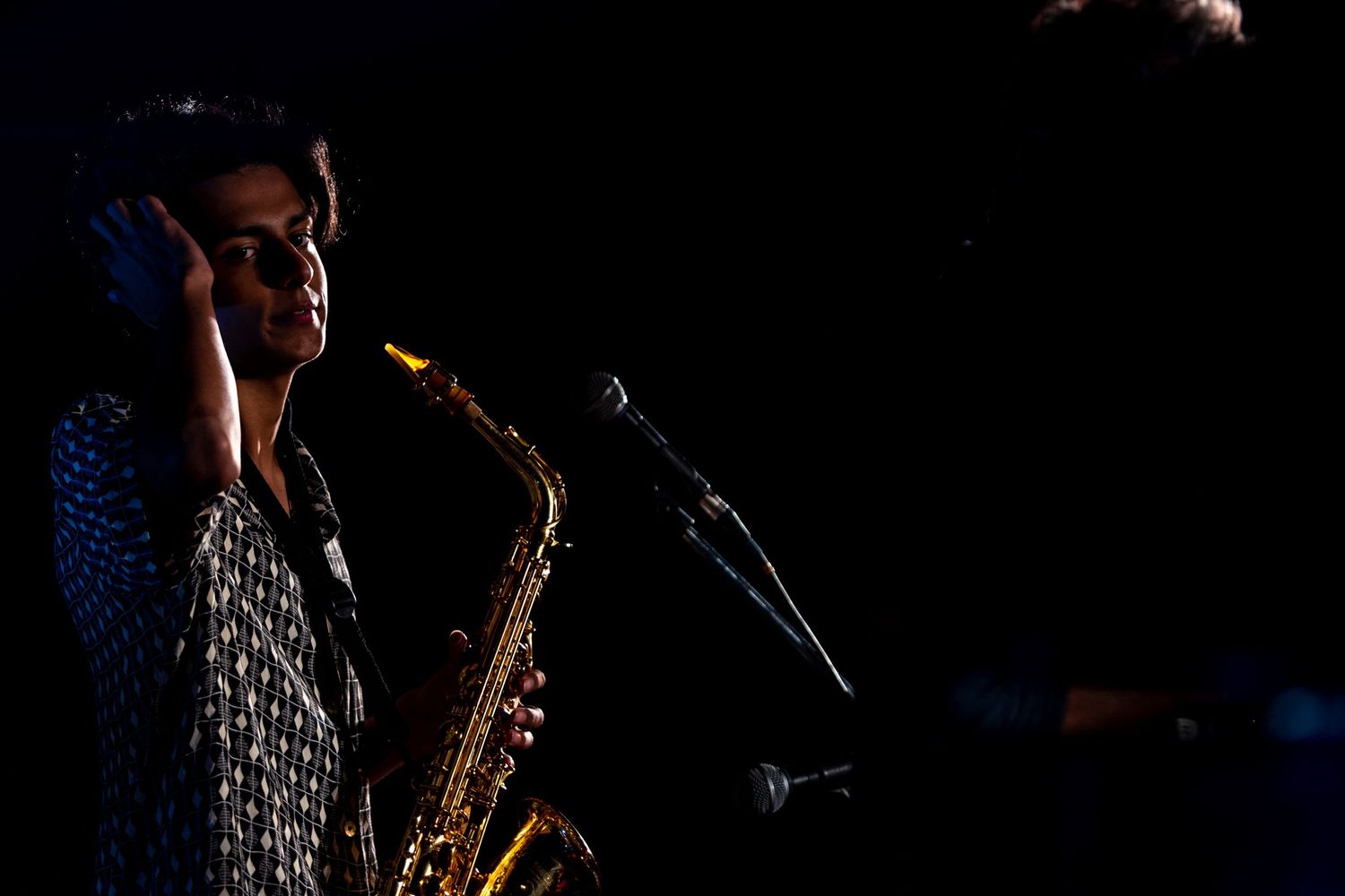 Saxophonist performing in dramatic low-key lighting with microphone setup.