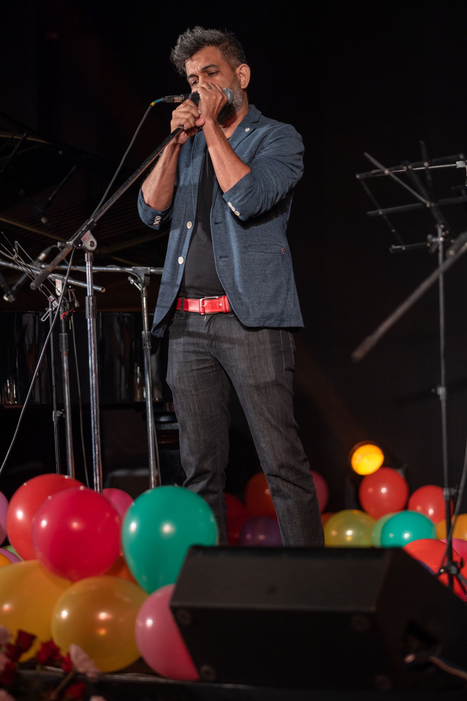 Performer singing into microphone on stage decorated with colorful balloons below.