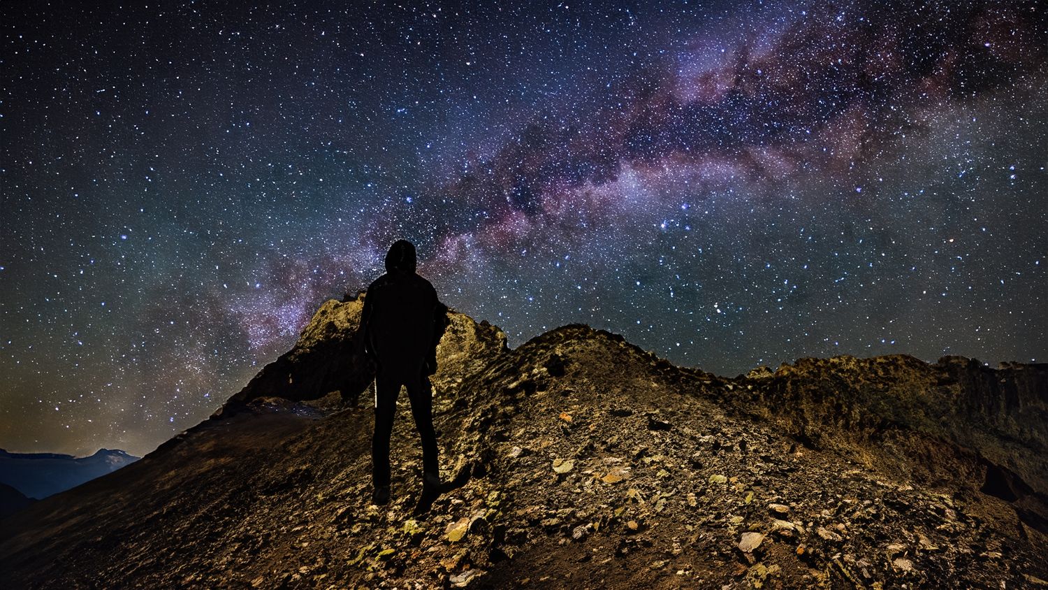 Milky Way galaxy stretches across the night sky above rugged mountain peaks in a stunning long exposure photograph.