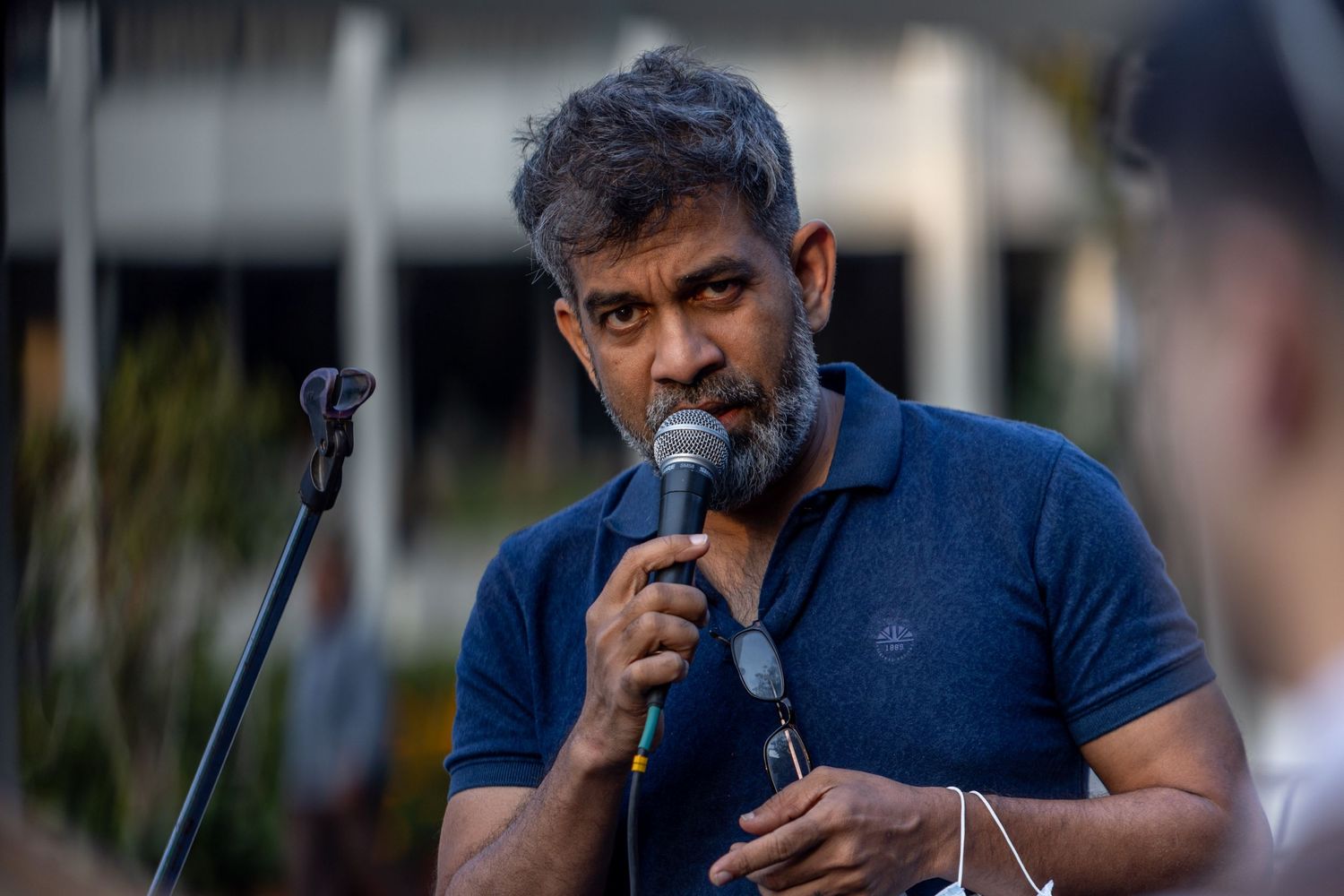 Performer sings into microphone during an outdoor concert at dusk.