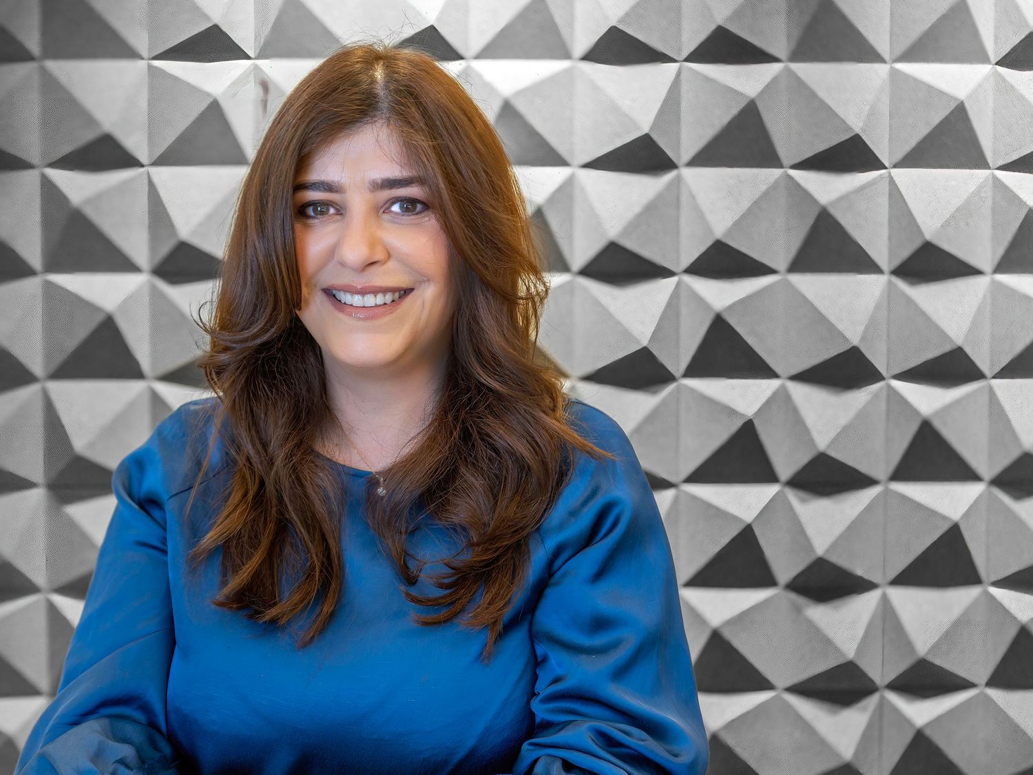 Professional portrait of woman in blue top against geometric patterned wall.