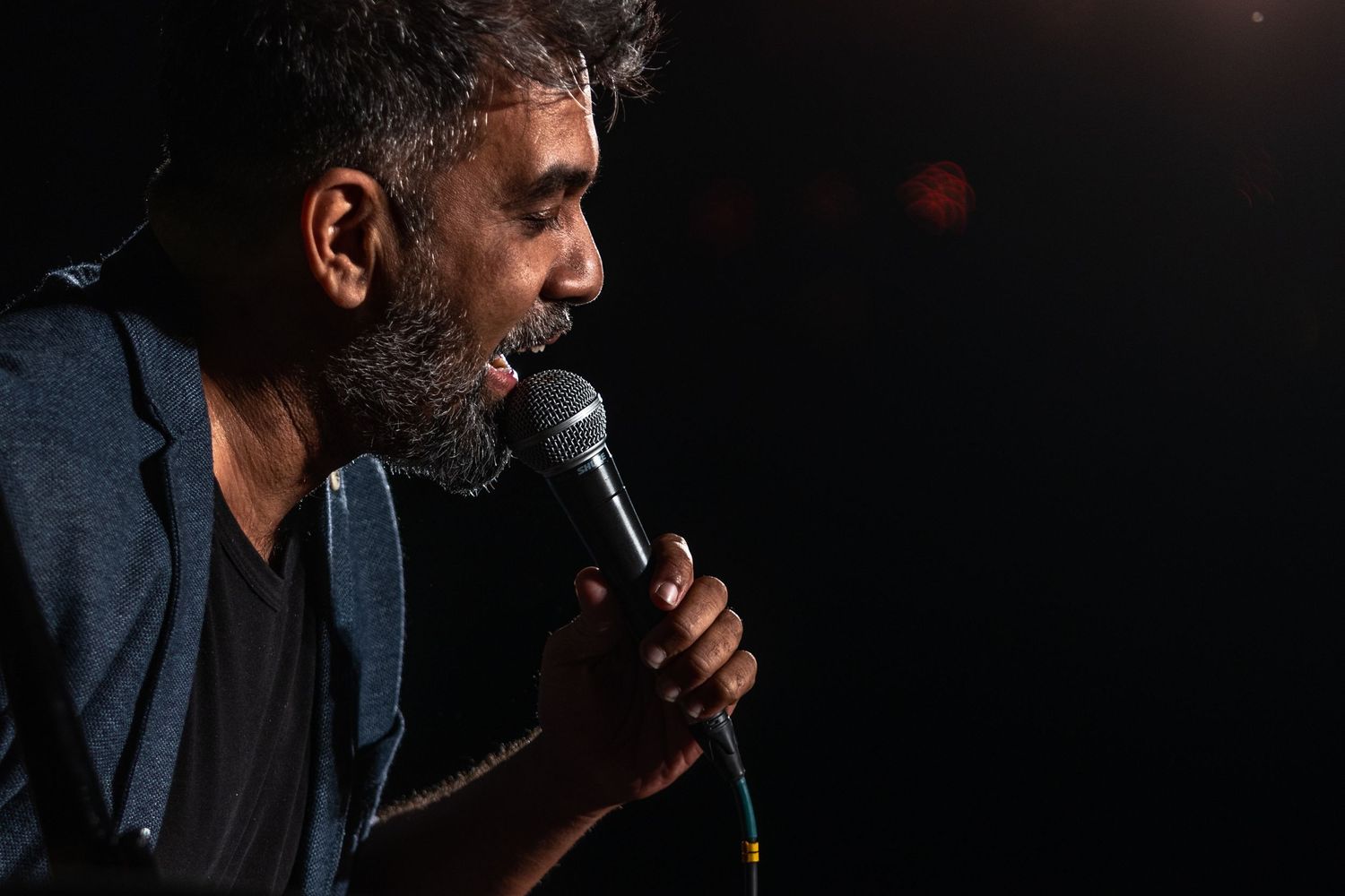 Close-up of performer singing into microphone with dramatic side lighting on dark stage.