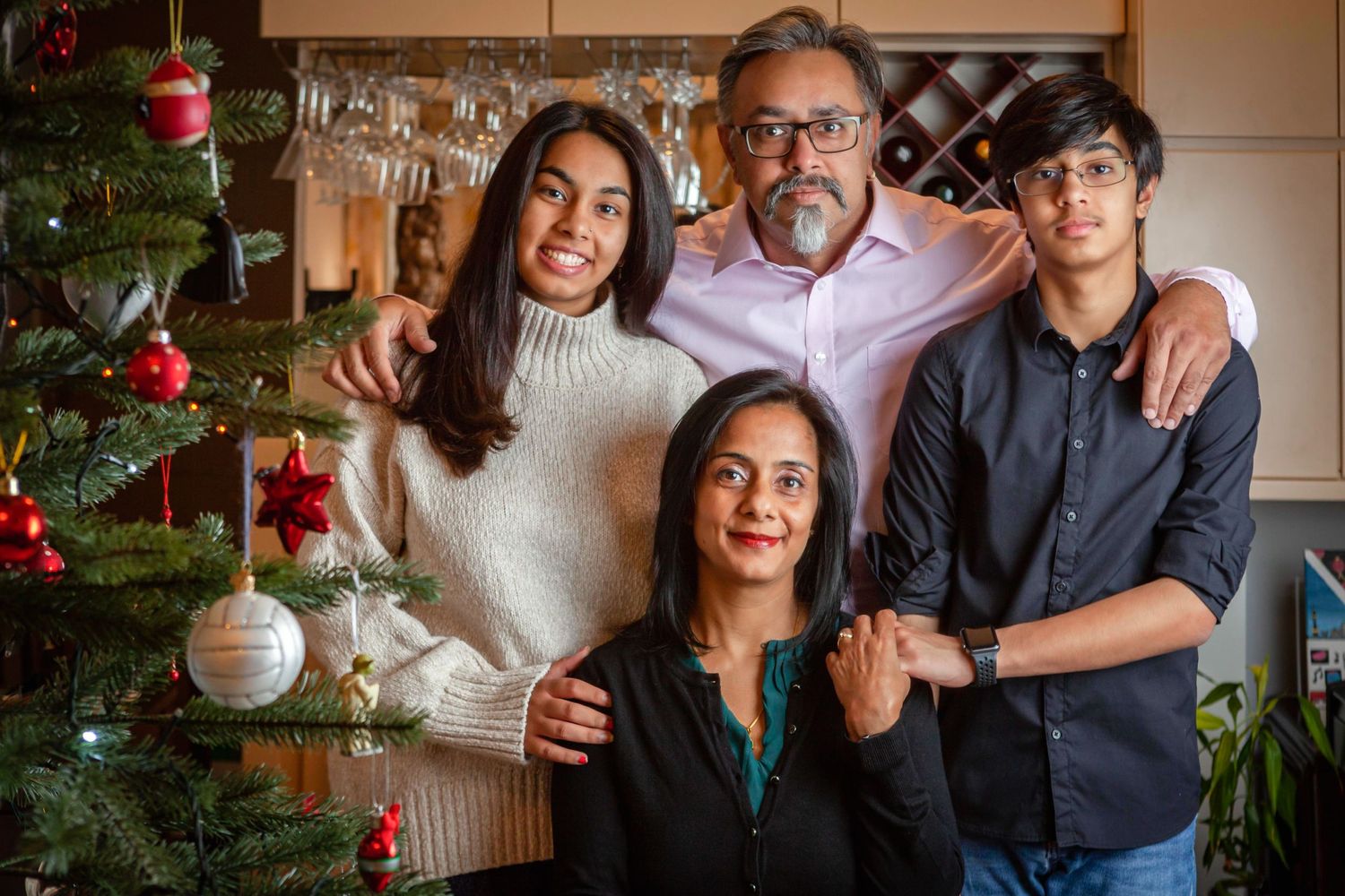 A family poses together for holiday portraits in front of a decorated Christmas tree in a cozy living room setting.