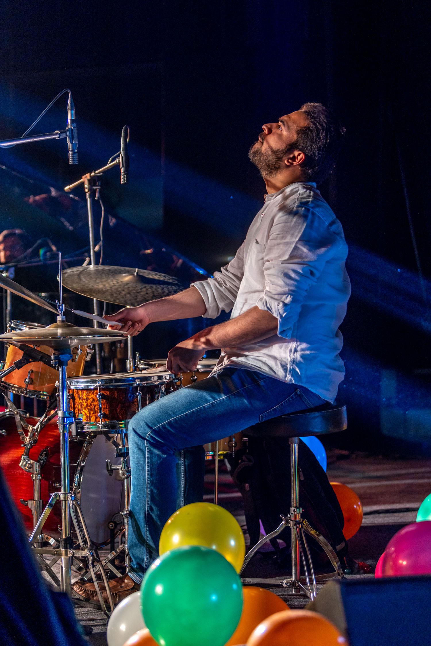 Drummer performing passionately on stage with colorful balloons decorating the foreground.