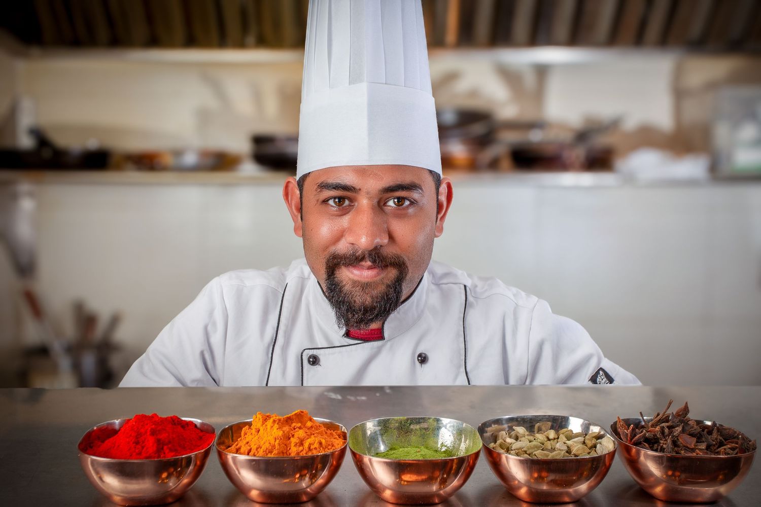 A professional chef in white uniform prepares ingredients in a commercial kitchen setting.