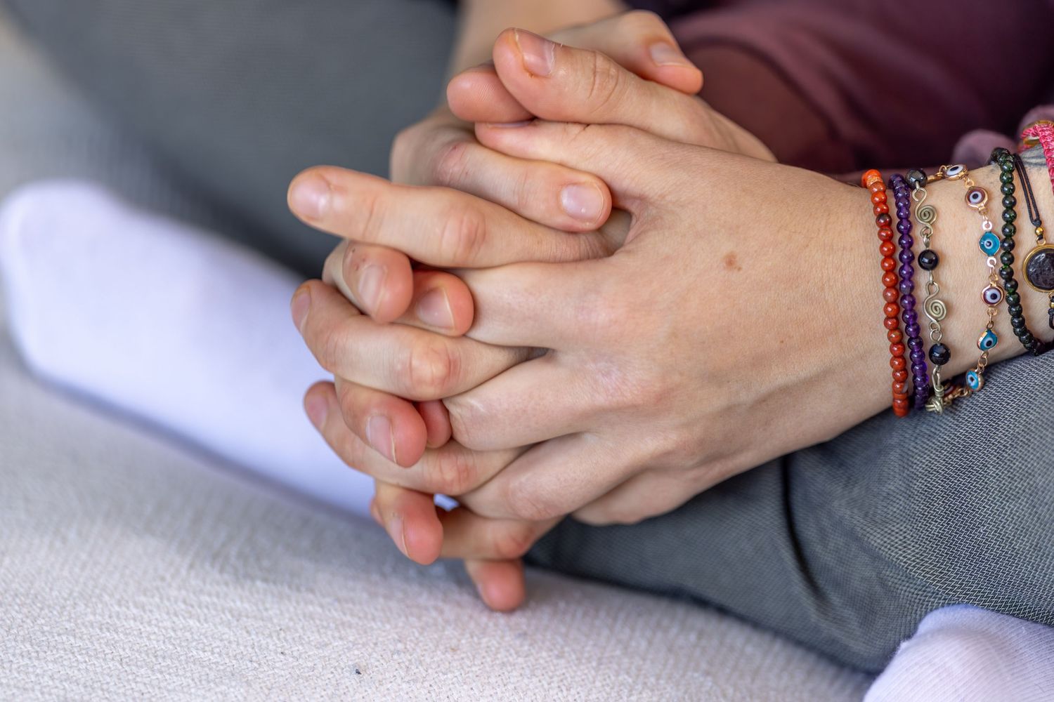Two people clasping hands together, one wearing colorful beaded bracelets, symbolizing support and connection.