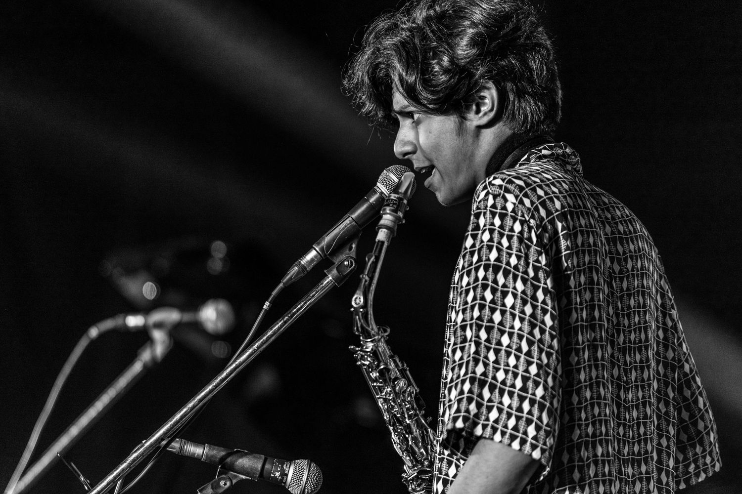 Black and white photo of saxophone player performing on stage with dramatic lighting.