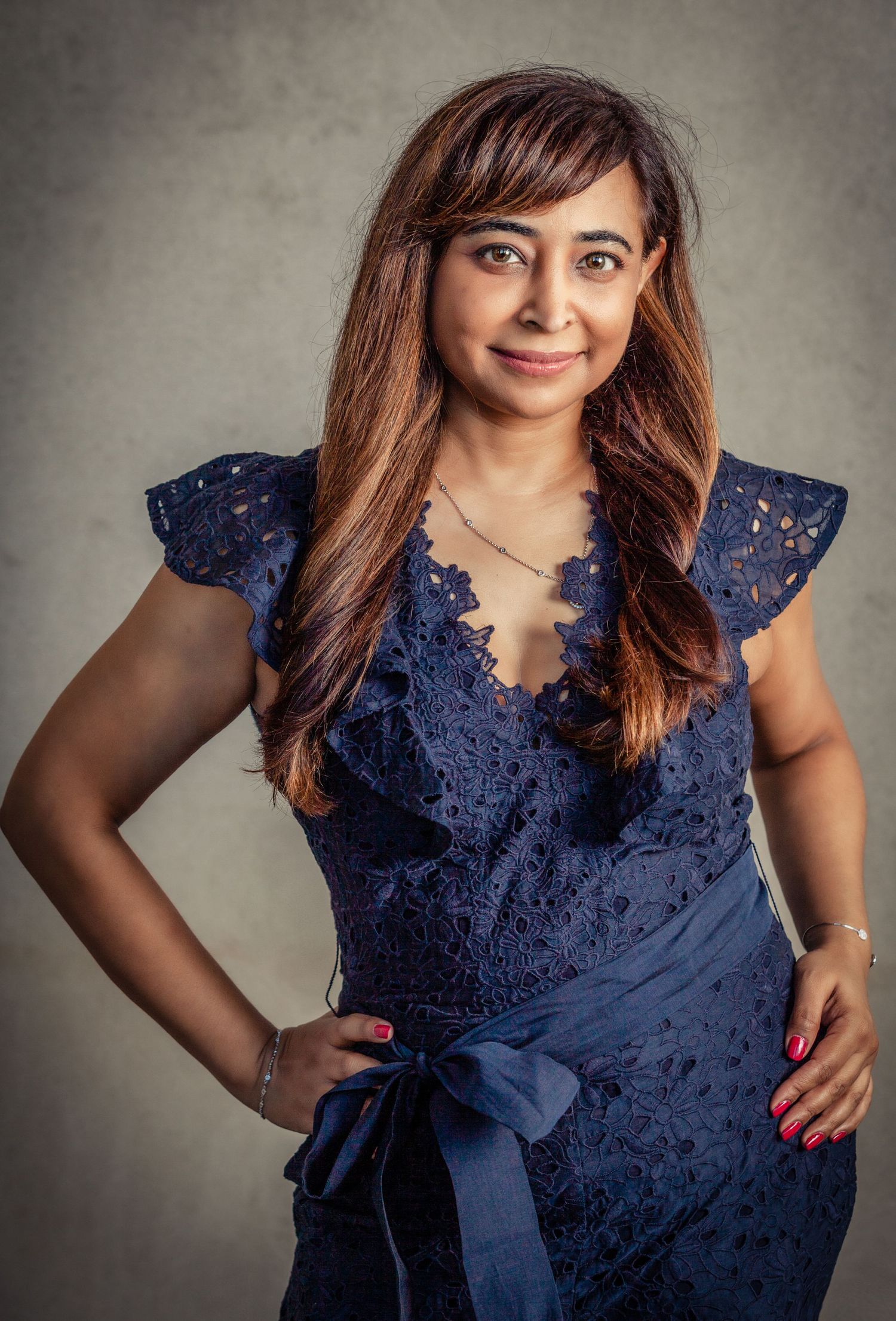 A series of portraits showing a person in a navy blue lace dress with flutter sleeves posing against a gray backdrop.