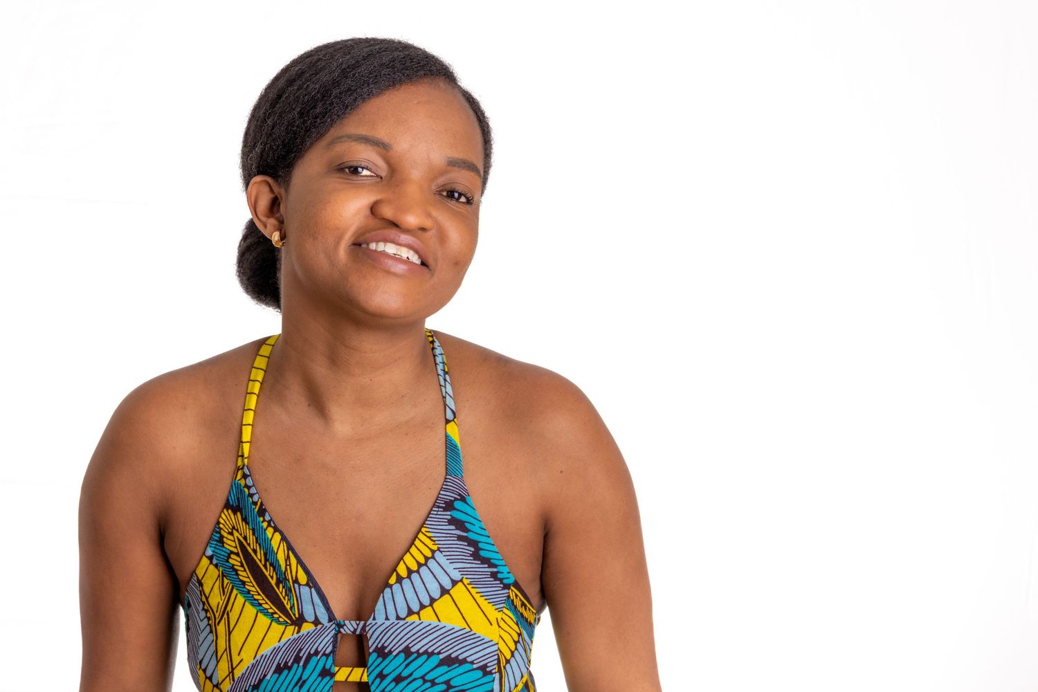 Woman wearing colorful patterned halter top with yellow and blue design smiles against white background.