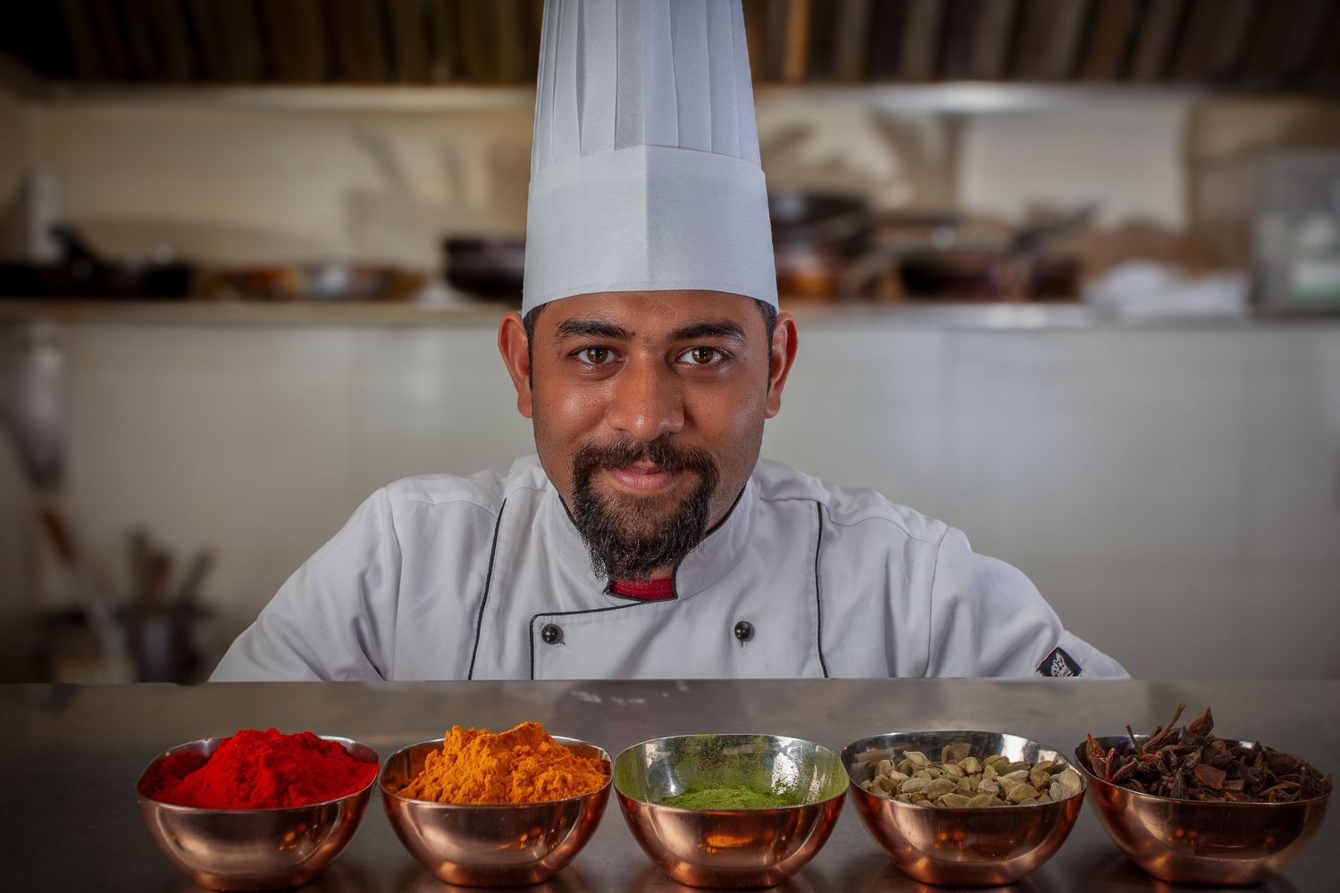 Row of chefs preparing food in commercial kitchen with various ingredients displayed.