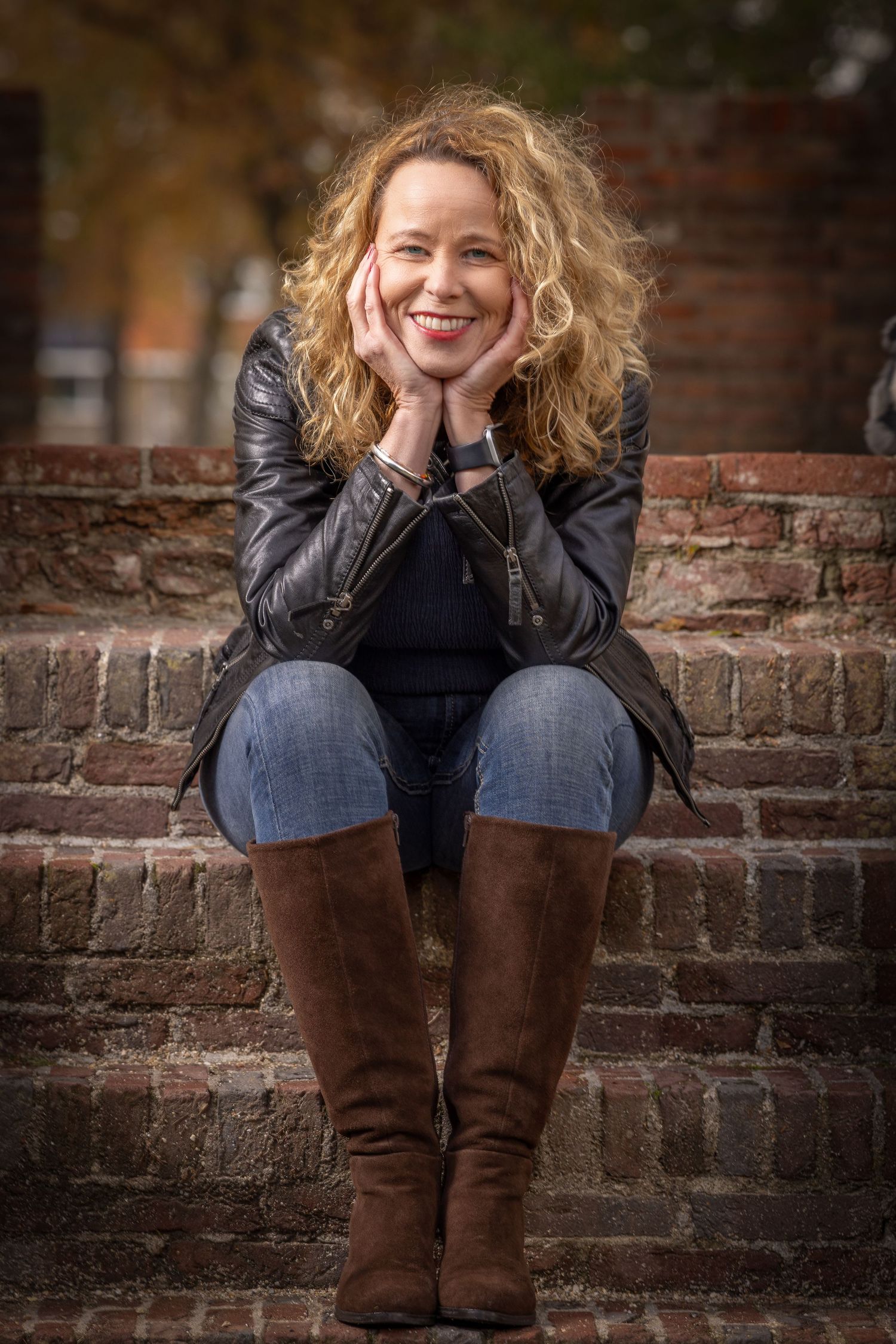 Person in brown boots and black jacket sits on brick steps in series of casual outdoor portraits.