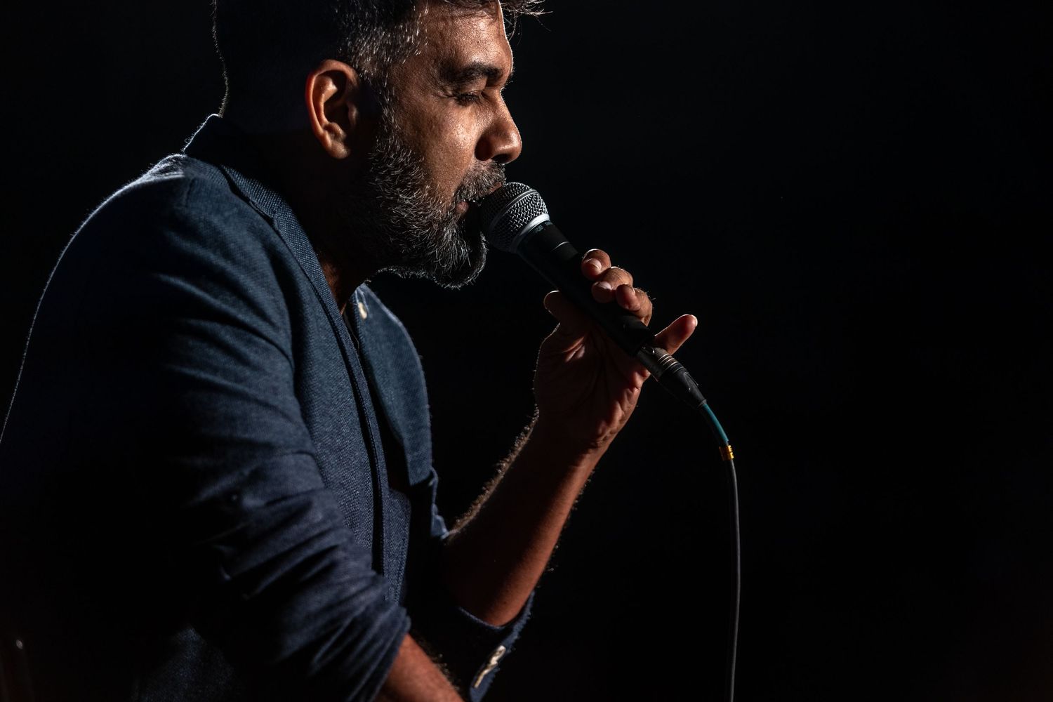 Profile view of performer singing into microphone against black background.