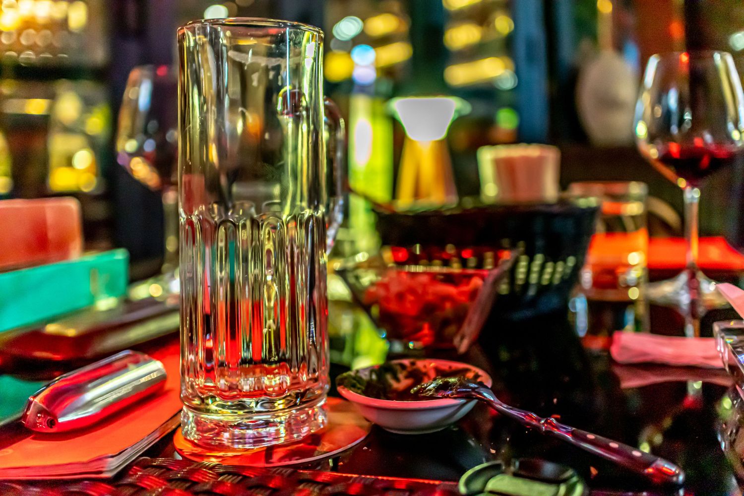 Empty beer mug and wine glasses on restaurant table with colorful ambient lighting.