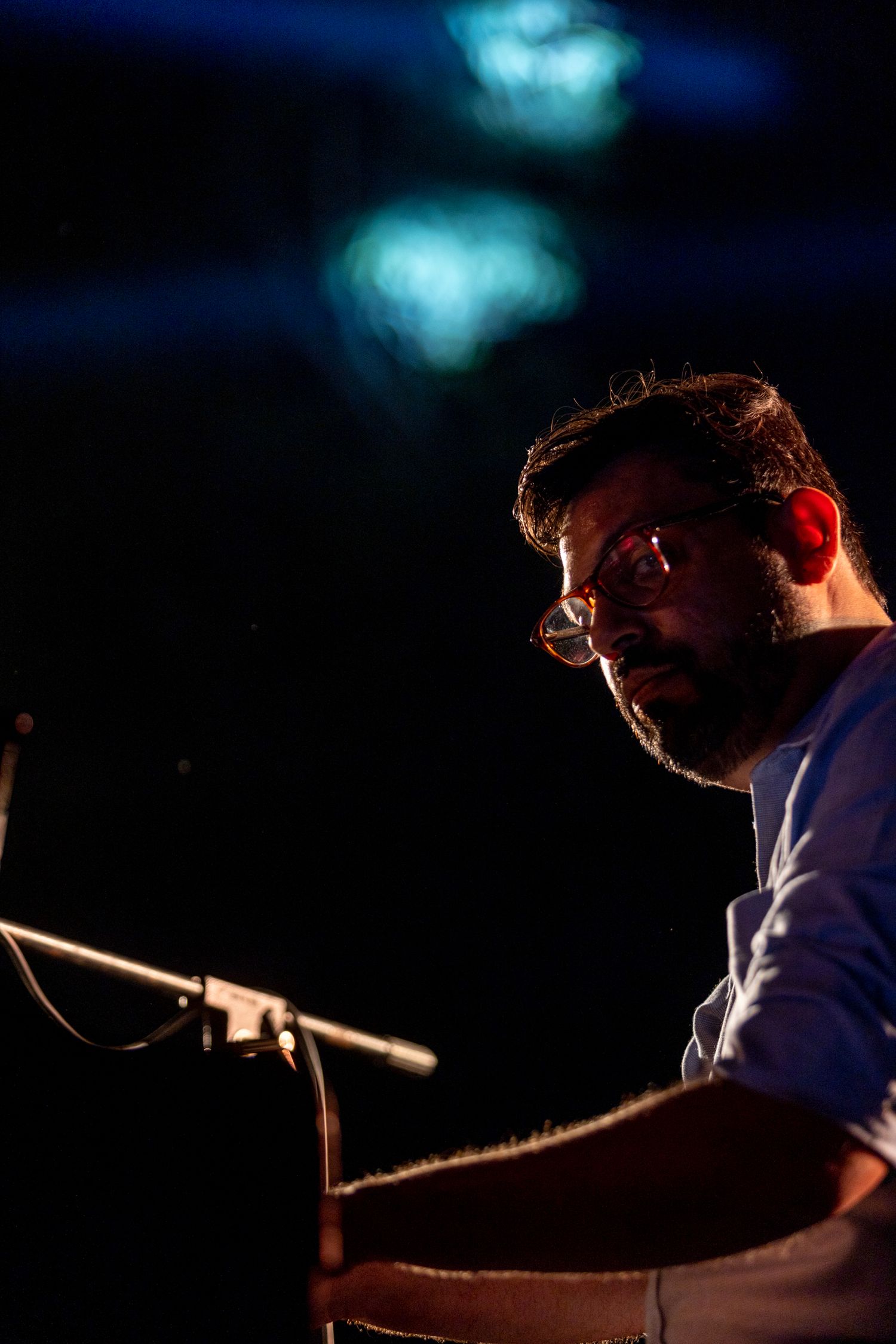 Profile shot of musician at piano with blue stage lights creating atmospheric mood.