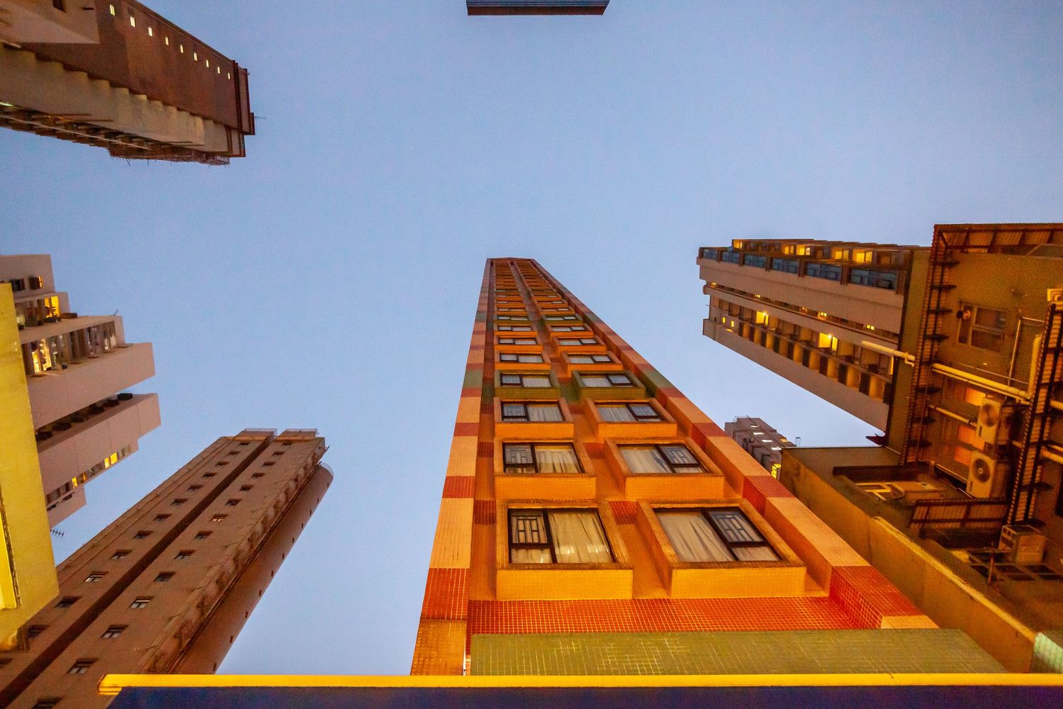 Low angle view of tall urban buildings converging toward blue sky.