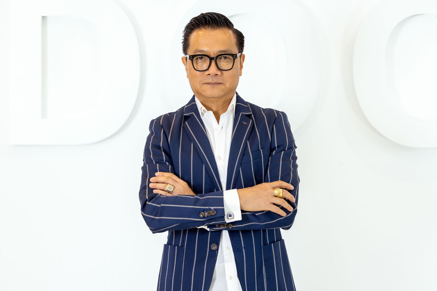 Professional in a navy pinstripe suit and glasses stands against a white background in multiple poses.