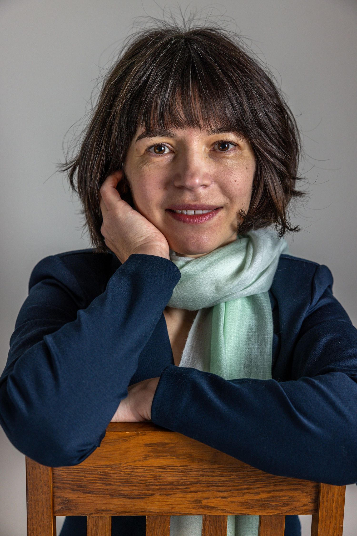 Person in navy sweater rests head on arms while wearing mint green scarf in progressive candid photo series.