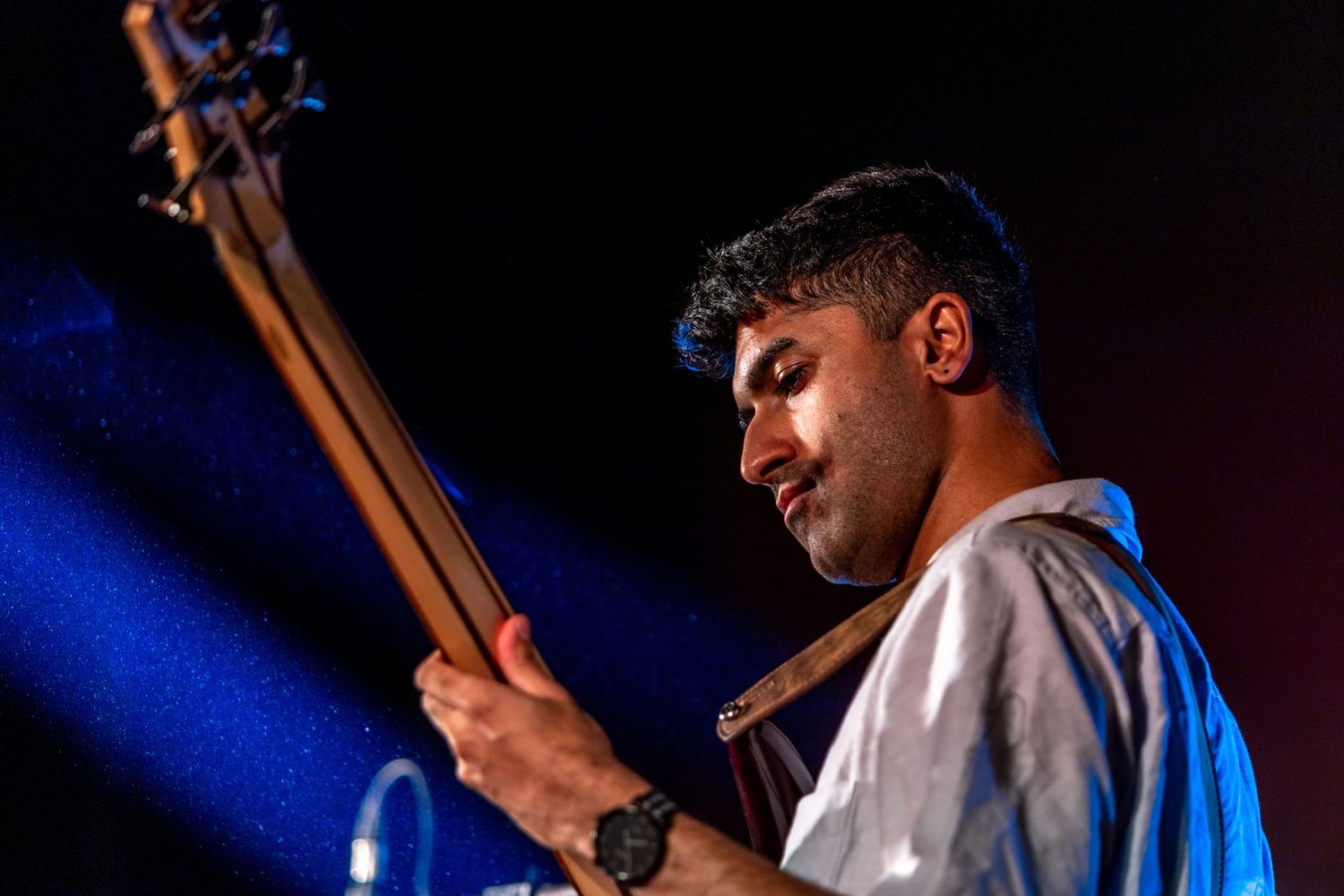 Bass player in white shirt illuminated by blue stage lights during performance.