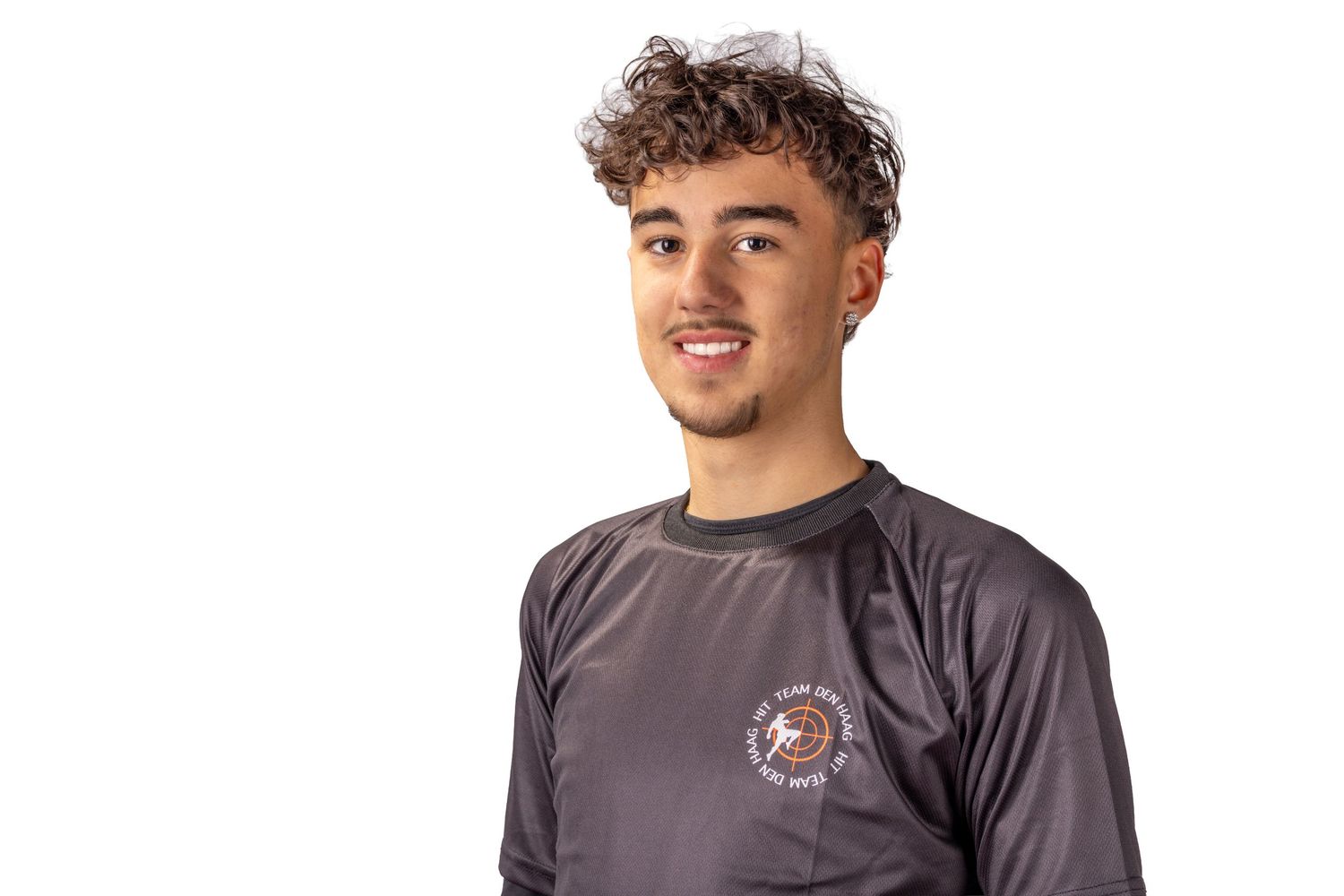 A person wearing a gray athletic shirt with curly hair smiles against a white background.