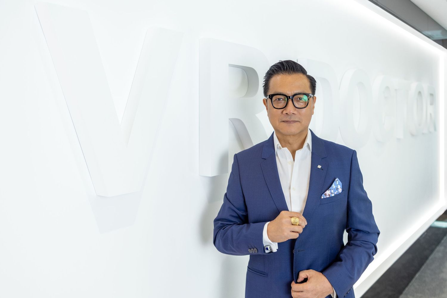 Professional wearing a navy blue suit and glasses poses confidently against a white background.
