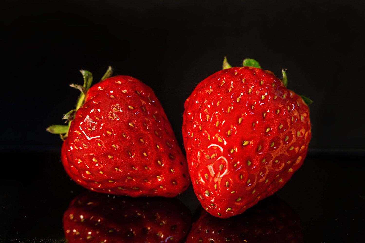 Close-up of two fresh red strawberries against a black background with reflective surface.