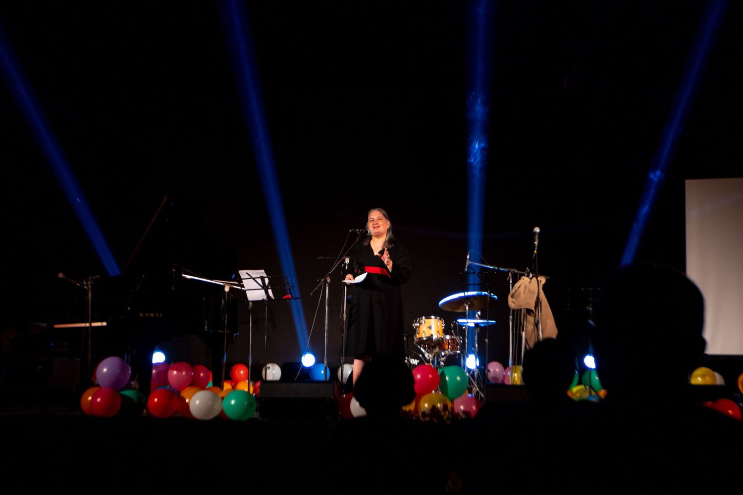 Performer on stage with dramatic blue spotlights and colorful balloon decorations.