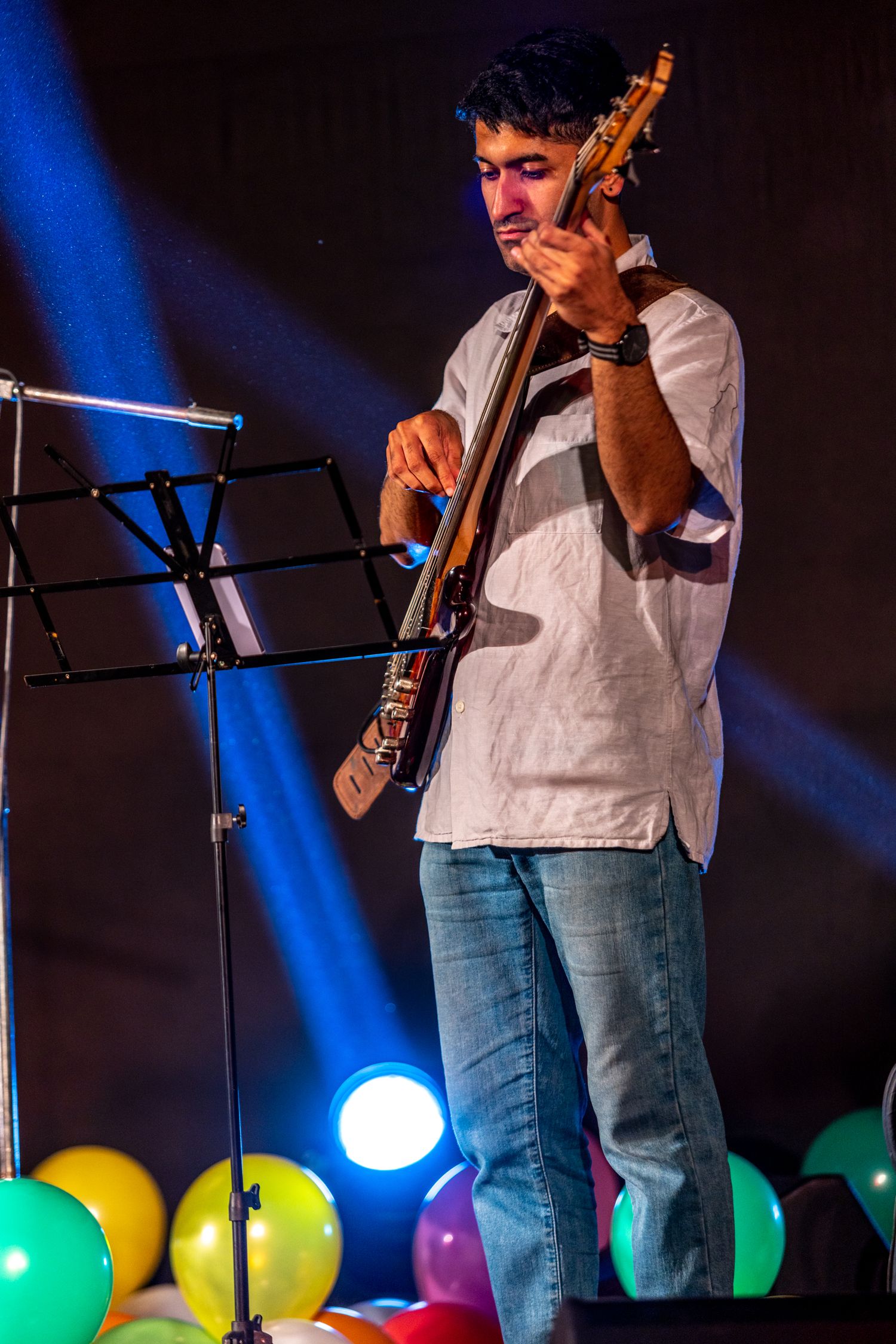 Bass guitarist performing on stage with colorful balloons and blue lighting effects.
